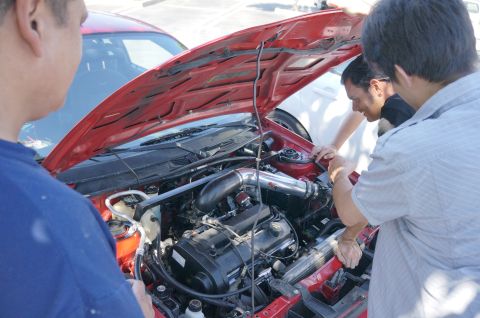 1995 Ford Taurus - People examine the engine bay of a red car, which has an aftermarket air intake system installed.