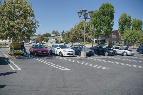 1995 Ford Taurus - A variety of vehicles are parked in a lot on a sunny day, with several hoods open.