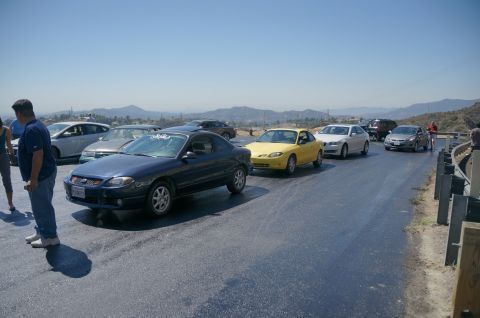1995 Ford Taurus - A line of cars are parked on a road with mountains in the background.