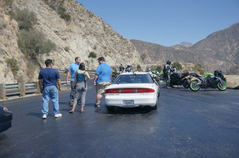 1995 Ford Taurus - A group of people and motorcycles are gathered on a scenic mountain road next to a white coupe.
