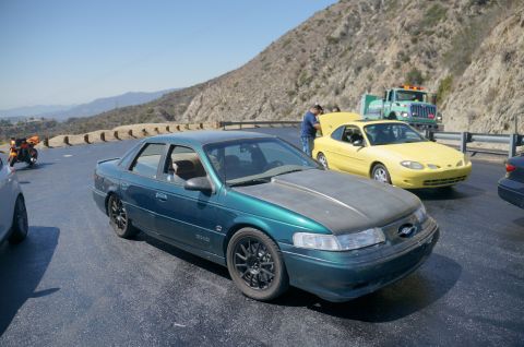 1995 Ford Taurus - A 1995 Ford Taurus and a yellow coupe are stopped on the side of a road, with a truck visible behind them.