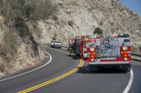 1995 Ford Taurus - Multiple emergency vehicles are stopped on a two-lane road next to a steep, dry hillside.