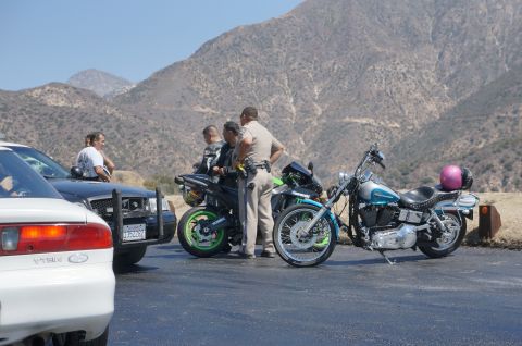 1995 Ford Taurus - Police officers interact with motorcyclists and drivers on a roadside with a mountainous backdrop.