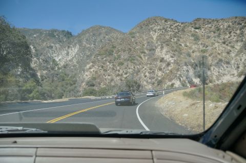 1995 Ford Taurus - Multiple vehicles navigate a scenic mountain highway on a sunny day.