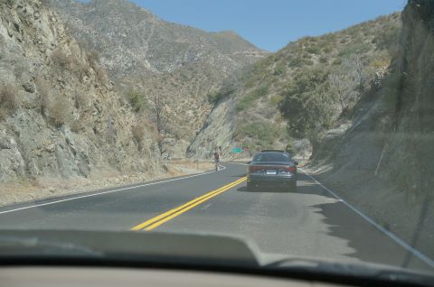 1995 Ford Taurus - A car travels down a winding road flanked by steep, rocky hillsides under a clear blue sky.