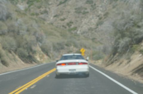 1995 Ford Taurus - A white sedan is seen from behind driving on a highway through a mountainous area.