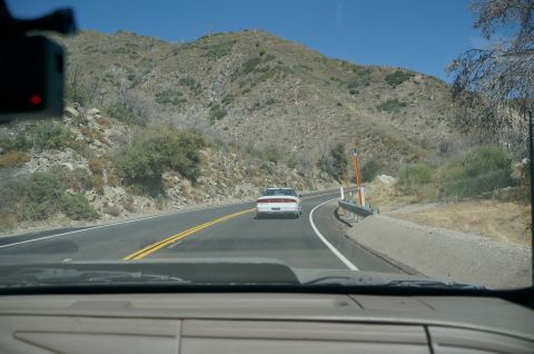 1995 Ford Taurus - A white sedan travels down a winding road in a dry, hilly landscape under a clear blue sky.