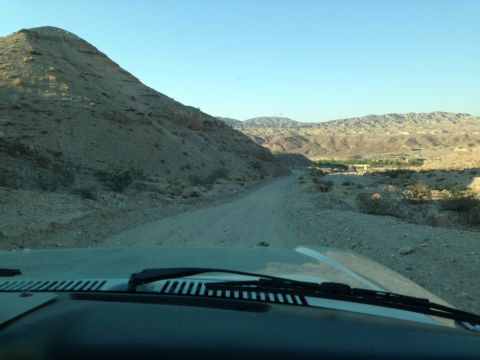 1986 Ford Bronco - Driving on a dusty desert road with mountains in the background, seen from the interior of a vehicle.