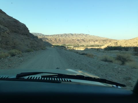 1986 Ford Bronco - Driving on a dirt road through a desert landscape with mountains under a clear blue sky.