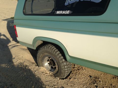 1986 Ford Bronco - This vintage Ford Bronco is partially buried in sand, with its rear tire deep in the loose terrain.