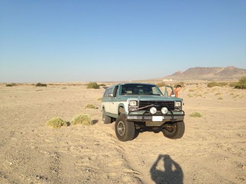1986 Ford Bronco - A two-tone green and white Ford Bronco is parked in a desert landscape with a person standing by the open door.