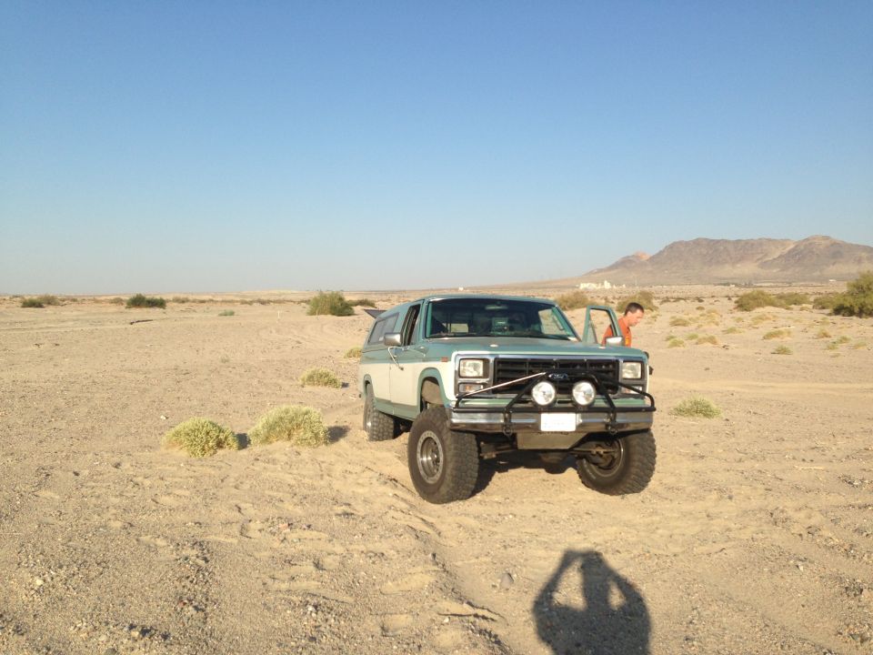 Two-tone green and white Ford Bronco with off-road lights and bull bar parked in a desert
