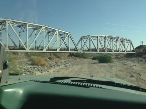1986 Ford Bronco - Driving towards a large truss bridge over a dry riverbed.