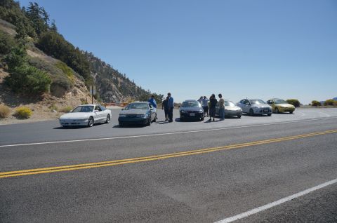 1995 Ford Taurus - A group of people stand around several cars parked on the side of a mountain road.
