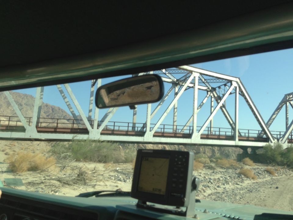 Interior view of a vehicle with a GPS unit, approaching a large metal bridge over a dry riverbed