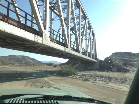 1986 Ford Bronco - Driving under a large railroad bridge in a desert environment.