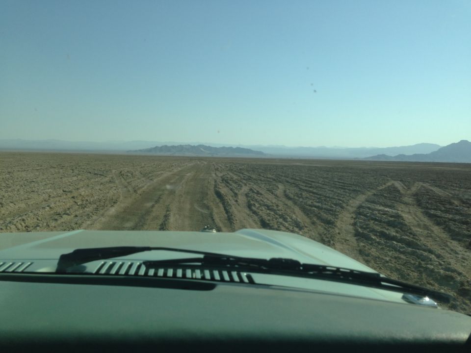 View from inside a vehicle looking out at a desert landscape with tire tracks