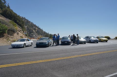 1995 Ford Taurus - A group of people gathered around several cars on a scenic mountain overlook.