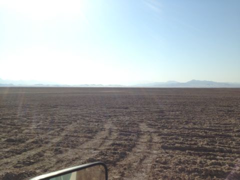 1986 Ford Bronco - A vast, dry landscape stretches to the horizon under a bright sky, marked by tire tracks.