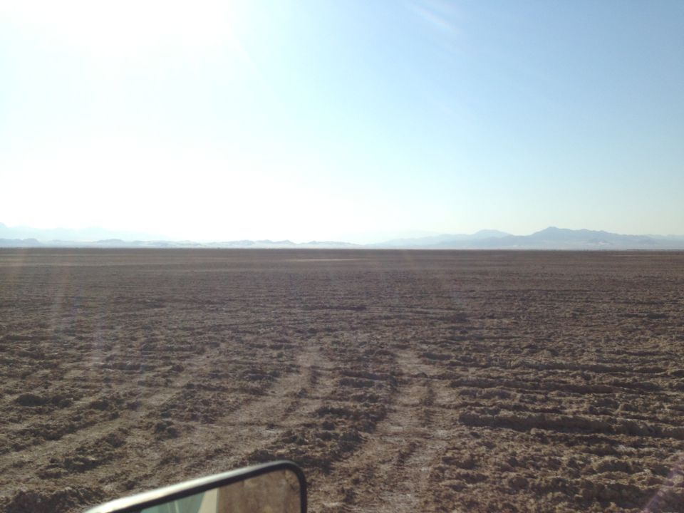 Desert landscape with tire tracks under a clear sky, seen from inside a vehicle