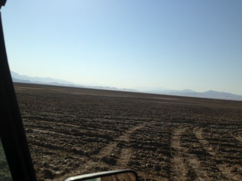1986 Ford Bronco - View from inside a vehicle traversing a dry, open terrain under a clear blue sky.