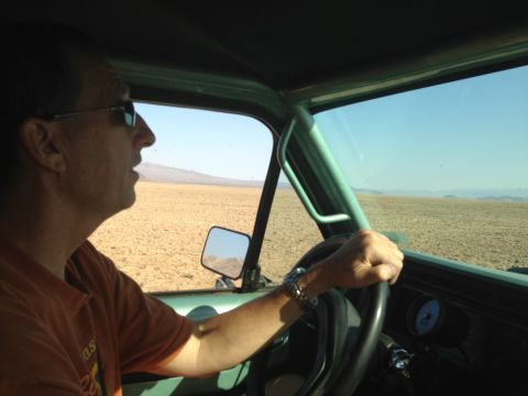 1986 Ford Bronco - A driver navigates a barren desert terrain under a clear blue sky.