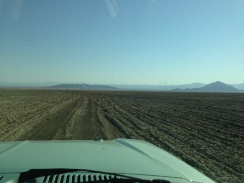 1986 Ford Bronco - View from inside a vehicle driving through a desolate, dry terrain with mountains in the distance.