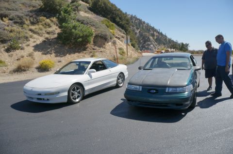 1995 Ford Taurus - A green 1995 Ford Taurus with a grey hood is parked next to a white Ford Probe on a sunny day.