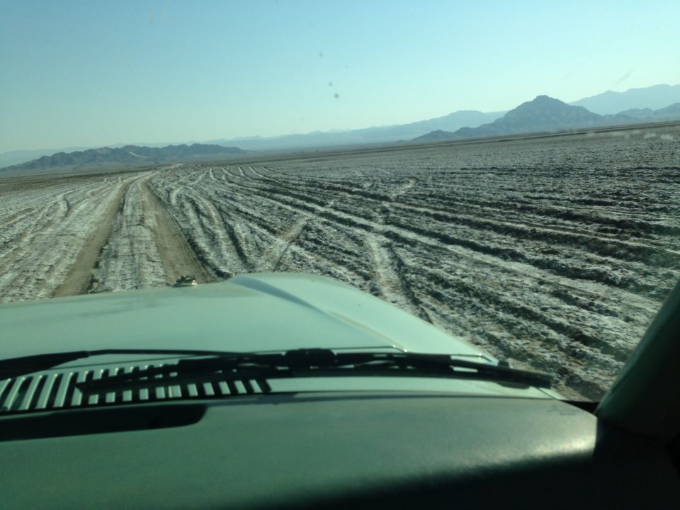 View from inside a vehicle driving on a dry lake bed with tire tracks