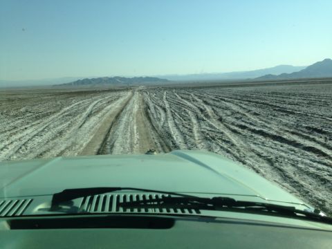 1986 Ford Bronco - View from inside a vehicle driving through a vast, dry desert landscape under a clear blue sky.