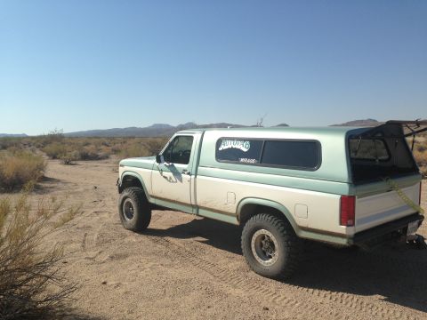 1986 Ford Bronco - This pickup truck, likely from the early 1980s, is parked in a dry, desert environment under a clear blue sky.
