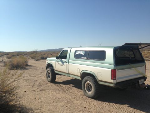 1986 Ford Bronco - Ford pickup truck with a camper shell in a desert landscape under a clear blue sky.
