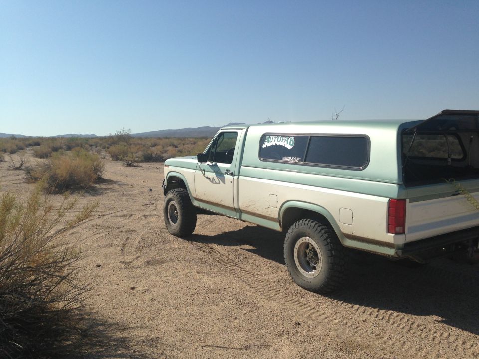 Pickup truck with camper shell parked on dirt road in desert landscape. Sticker on window says 'AUTOTOP6 MIRAGE'