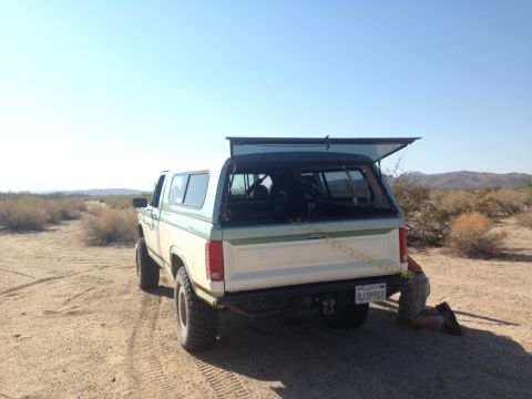 1986 Ford Bronco - Ford Bronco in desert landscape, rear view with camper shell open.
