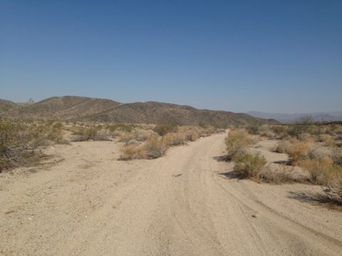 1986 Ford Bronco - A dirt road cuts through a dry, arid landscape with sparse vegetation and rolling hills in the distance.