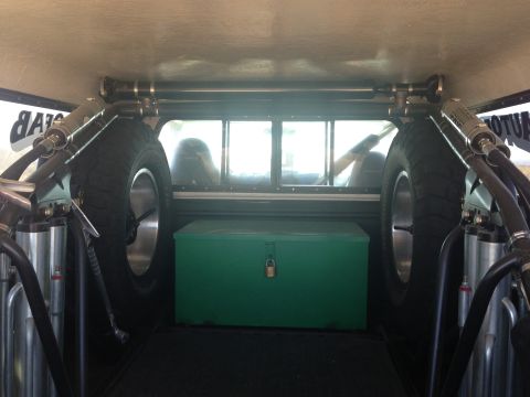 1986 Ford Bronco - The rear interior of a vehicle shows two spare tires, a green toolbox, and parts of the suspension system.