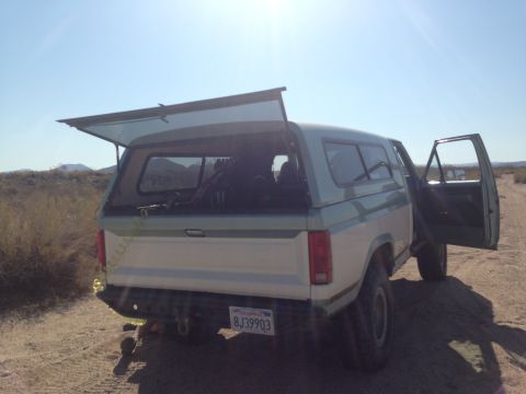 1986 Ford Bronco - This Ford Bronco, likely from the early 1980s, is parked in a desert landscape with its rear hatch and driver door open.