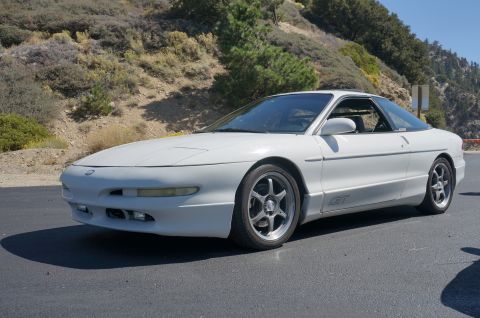 1995 Ford Taurus - A white coupe with a GT badge is parked on the side of a road with a mountainous backdrop.