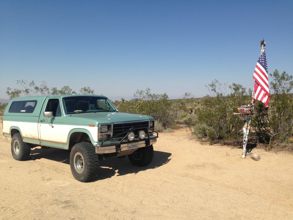 Green and white pickup truck with camper shell and off-road tires parked in desert landscape