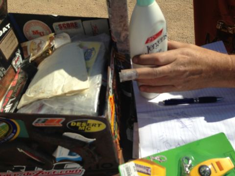 1986 Ford Bronco - Box with various stickers and contents, a hand holds a lotion bottle over a notebook.