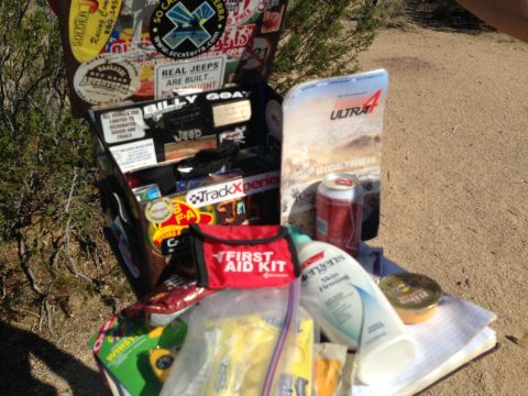 1986 Ford Bronco - A collection of items, including a first aid kit and various stickers, are gathered outdoors on a sandy surface.