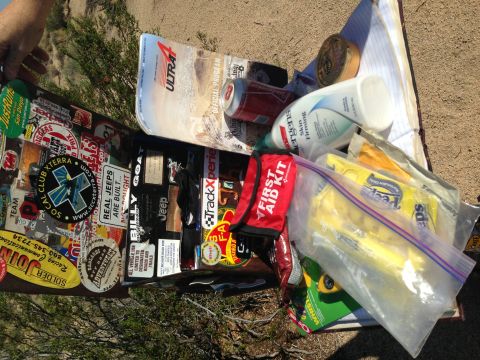 1986 Ford Bronco - A collection of items, including numerous stickers, a soda can, and a first aid kit, are spread out on a sandy surface.