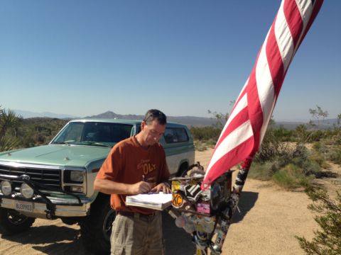 1986 Ford Bronco - A man signs a logbook next to a vintage SUV in a desert landscape.