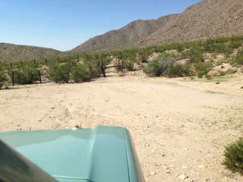 1986 Ford Bronco - The view from inside a vehicle shows a dusty track leading through a desert landscape towards a distant mountain range.