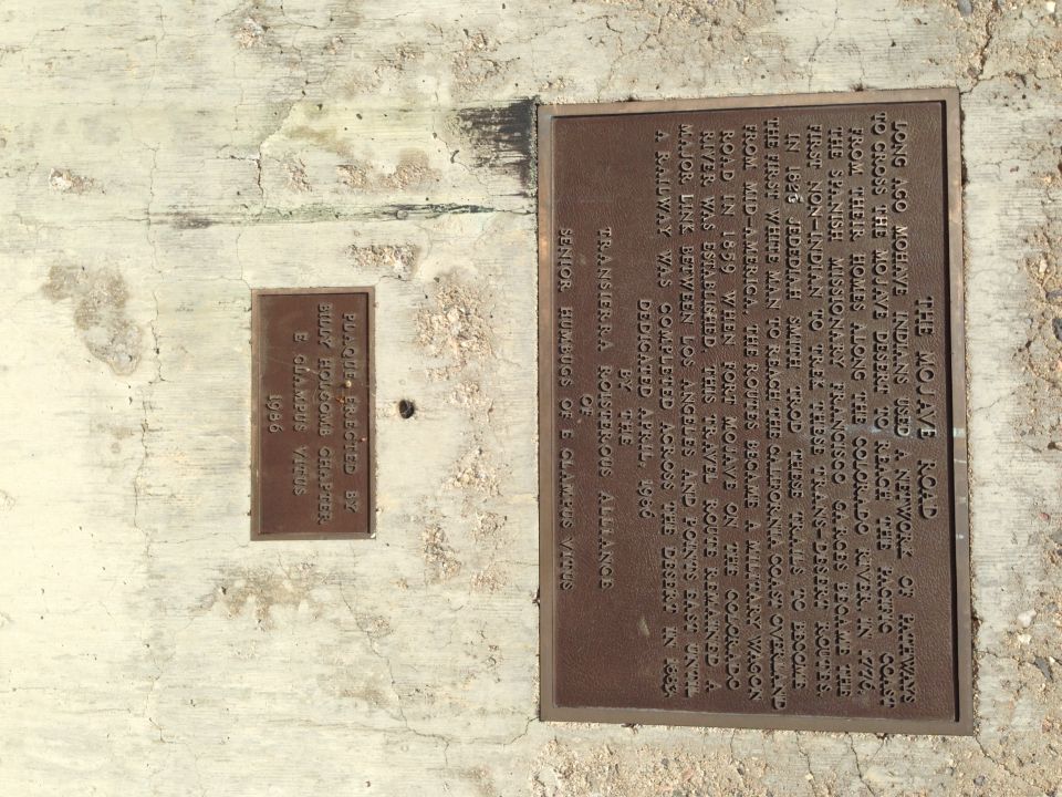 Two historical markers on a concrete wall, one detailing the Mojave Road, the other a dedication from 1986
