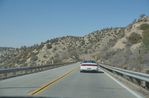 1995 Ford Taurus - A white 1995 Ford Taurus travels down a highway through a mountainous, arid landscape.