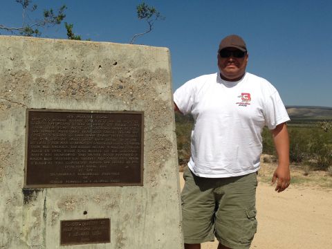 1986 Ford Bronco - A man poses next to a monument detailing the history of the Mojave Trail in a desert environment.