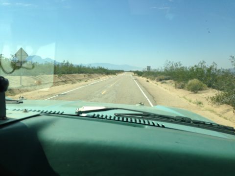 1986 Ford Bronco - View from inside a vehicle driving on a long, straight desert highway under a clear blue sky.