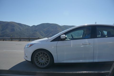 1995 Ford Taurus - White sedan driving on a highway with mountains in the distance under a clear blue sky.