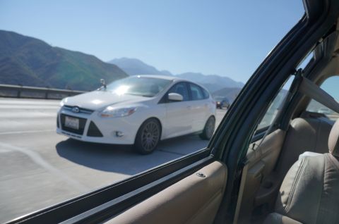 1995 Ford Taurus - A white Ford Focus hatchback is seen on the highway, with mountains in the distance.